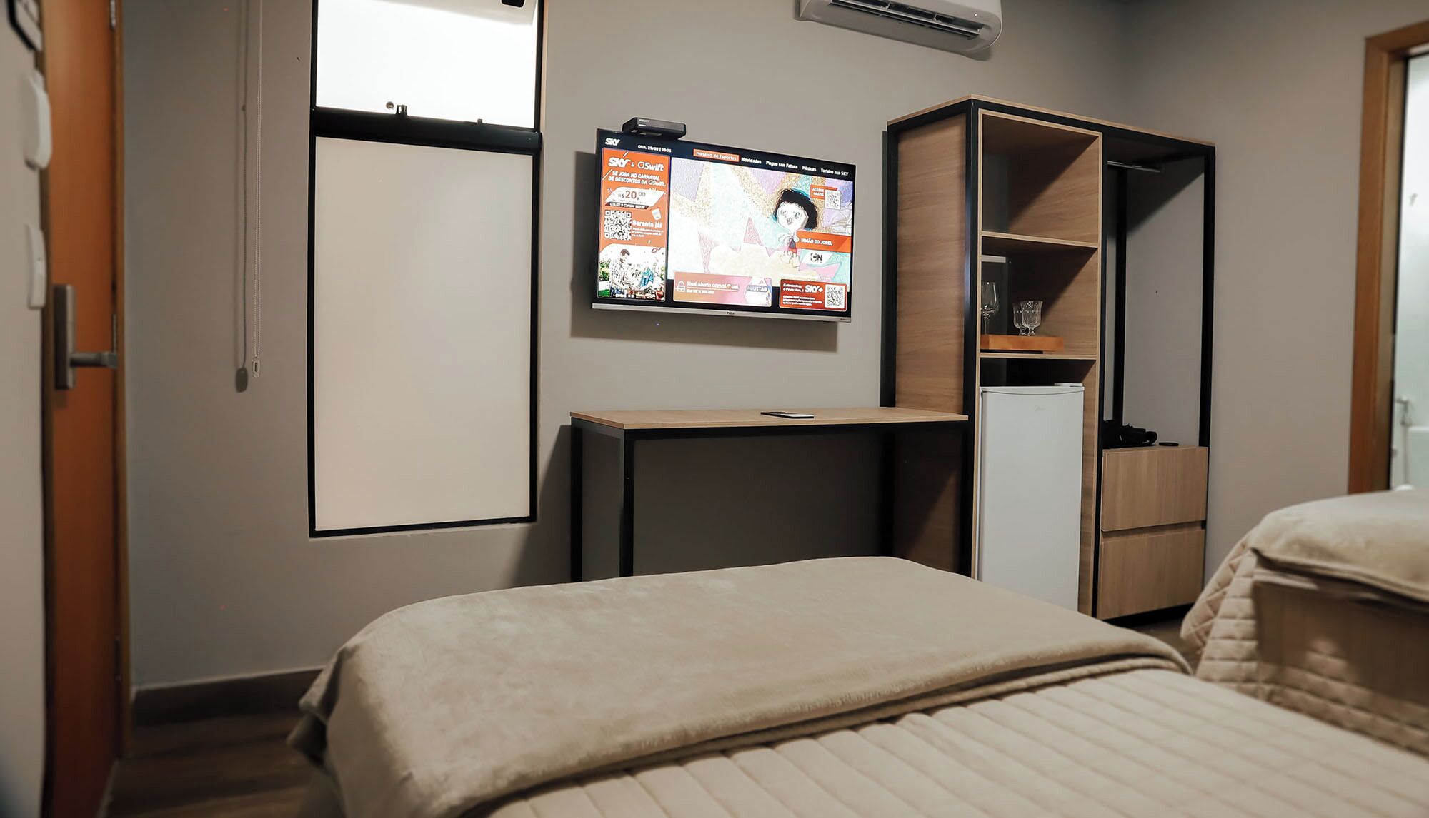A hotel room with a bed, a desk, a TV mounted on the wall, and a wardrobe.