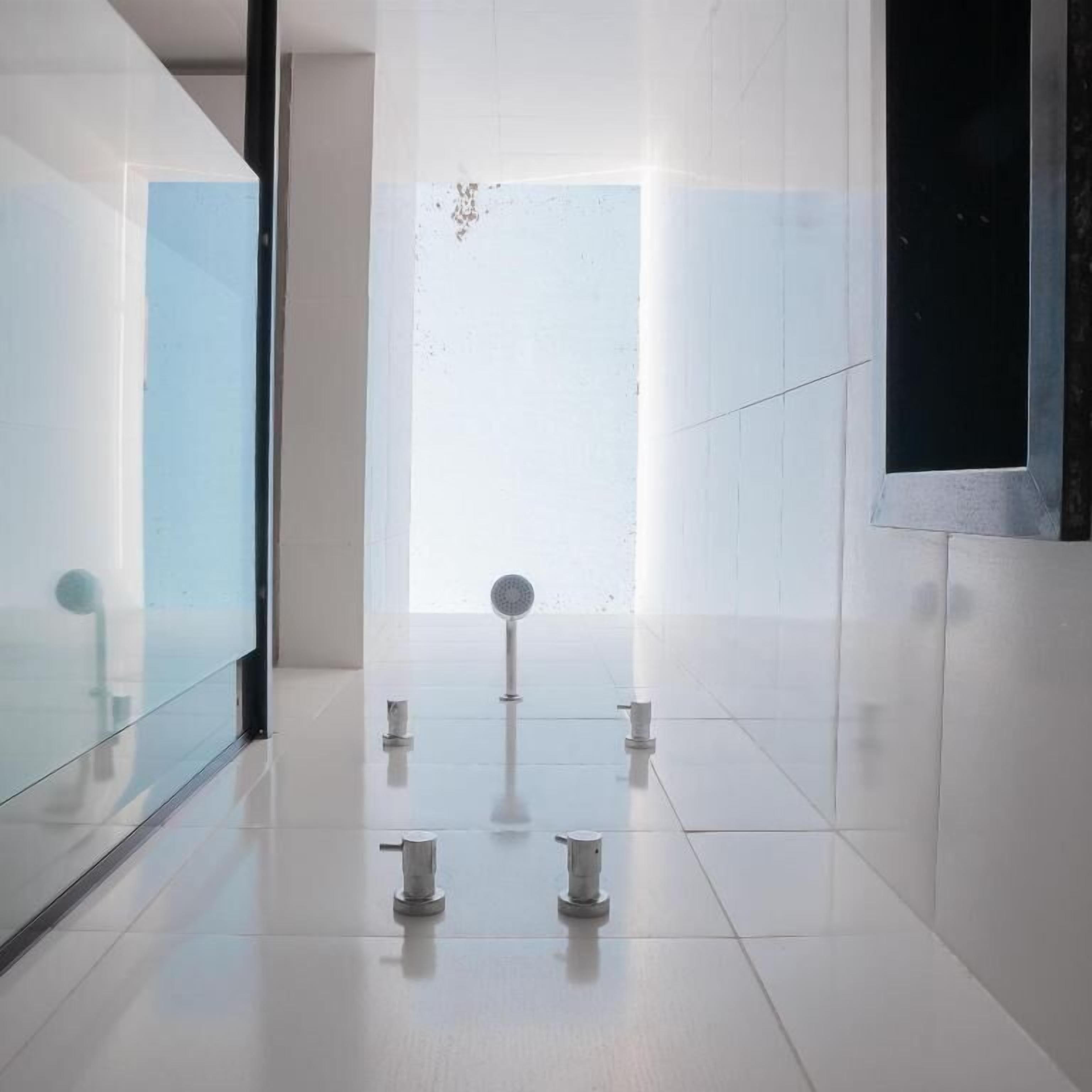 A modern, minimalist hallway with a glass wall on one side, a large window at the end, and a few metallic objects on the floor.
