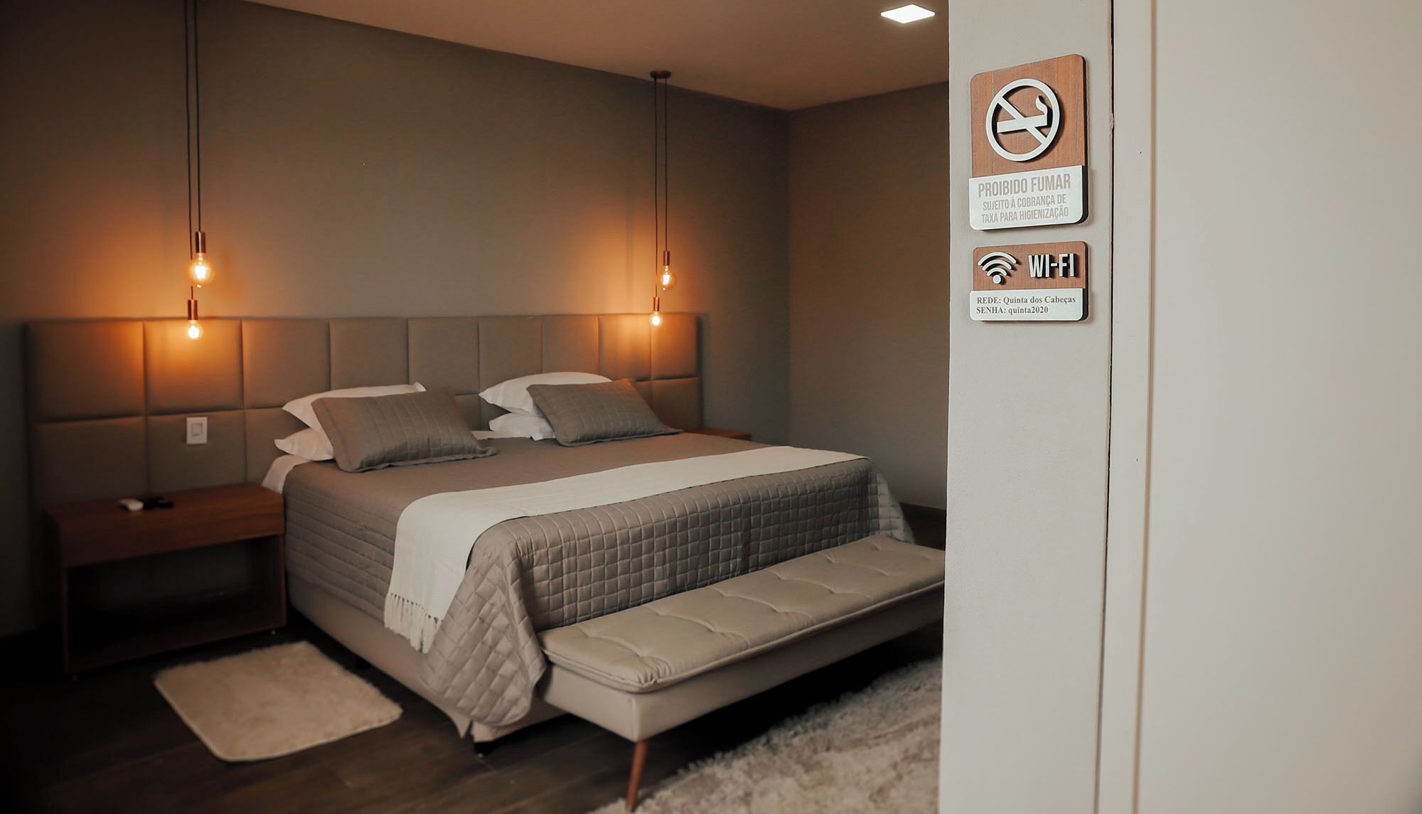 A modern bedroom with a bed, bedside tables, and a nightstand. There are two wall-mounted light fixtures above the bed.