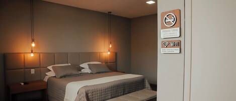 A modern bedroom with a bed, bedside tables, and a nightstand. There are two wall-mounted light fixtures above the bed.
