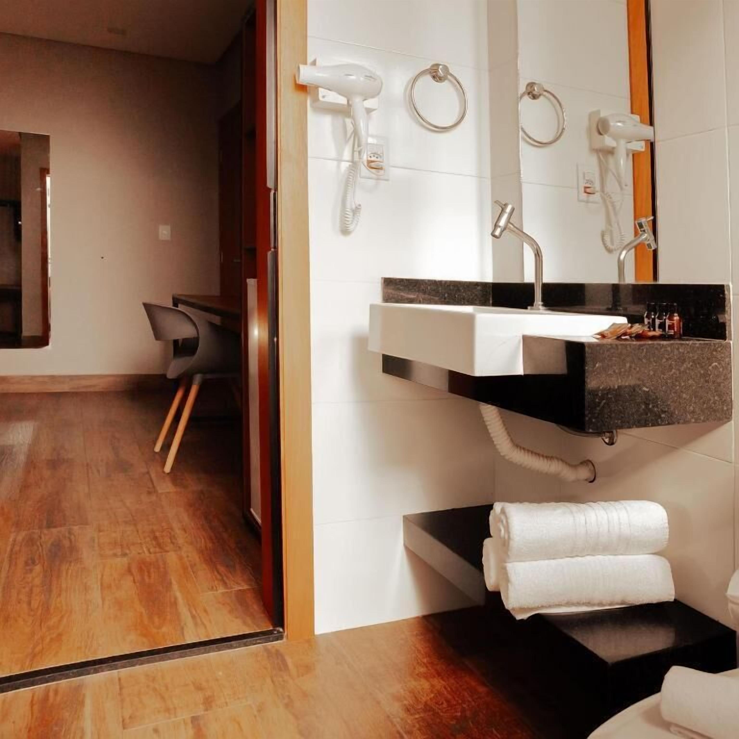 Un bagno moderno con lavabo su piano nero, uno specchio e due asciugacapelli fissati al muro.