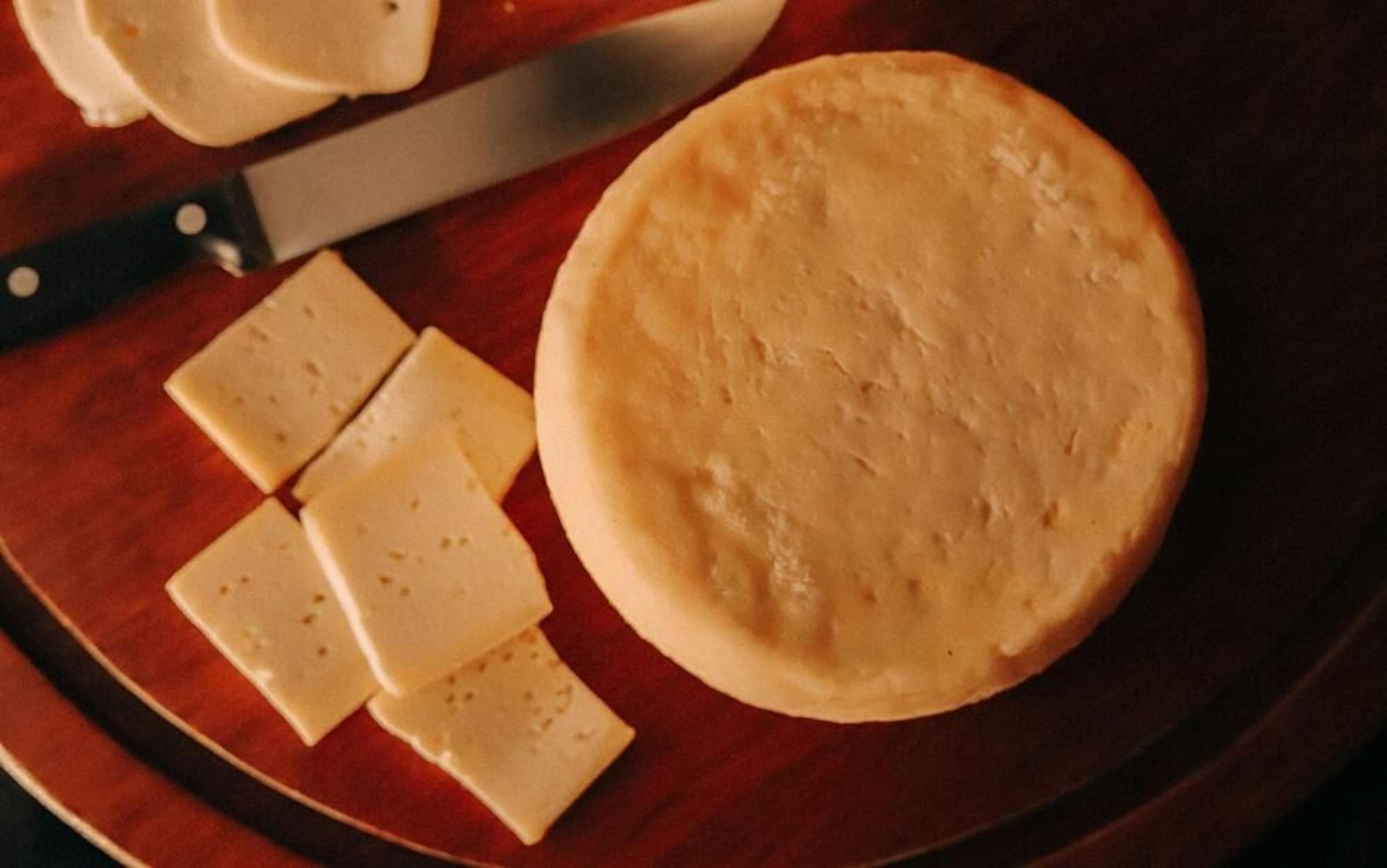 A cheese wheel and several cheese slices on a wooden board.