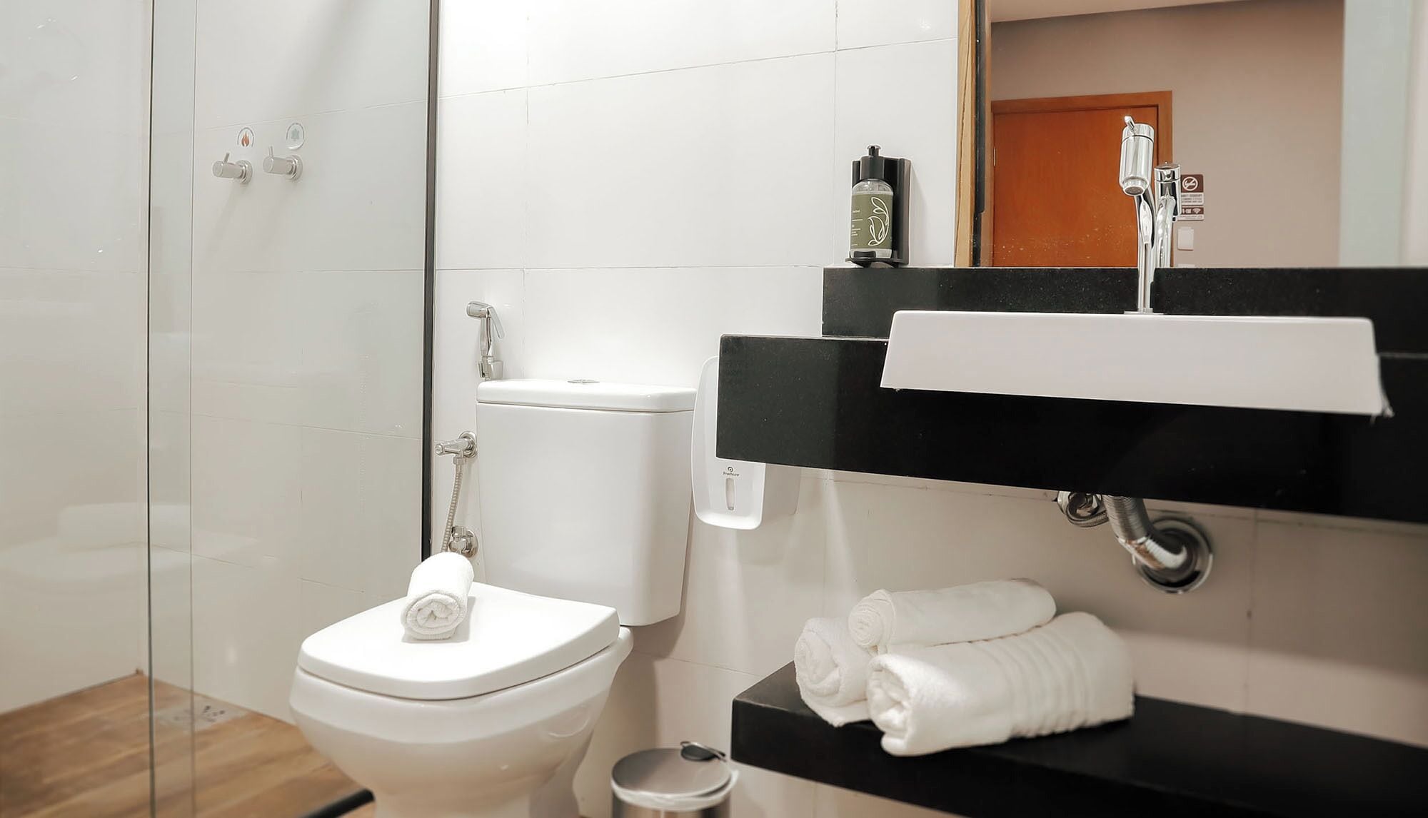 A modern bathroom with a glass shower enclosure, a white toilet, a black sink with a towel rack, and a mirror above the sink.