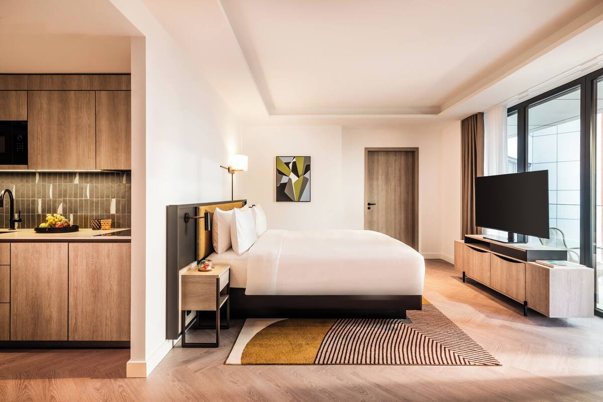 Una habitación de hotel moderna con cama, mesita de noche, lámpara, televisor y vistas a la ciudad.