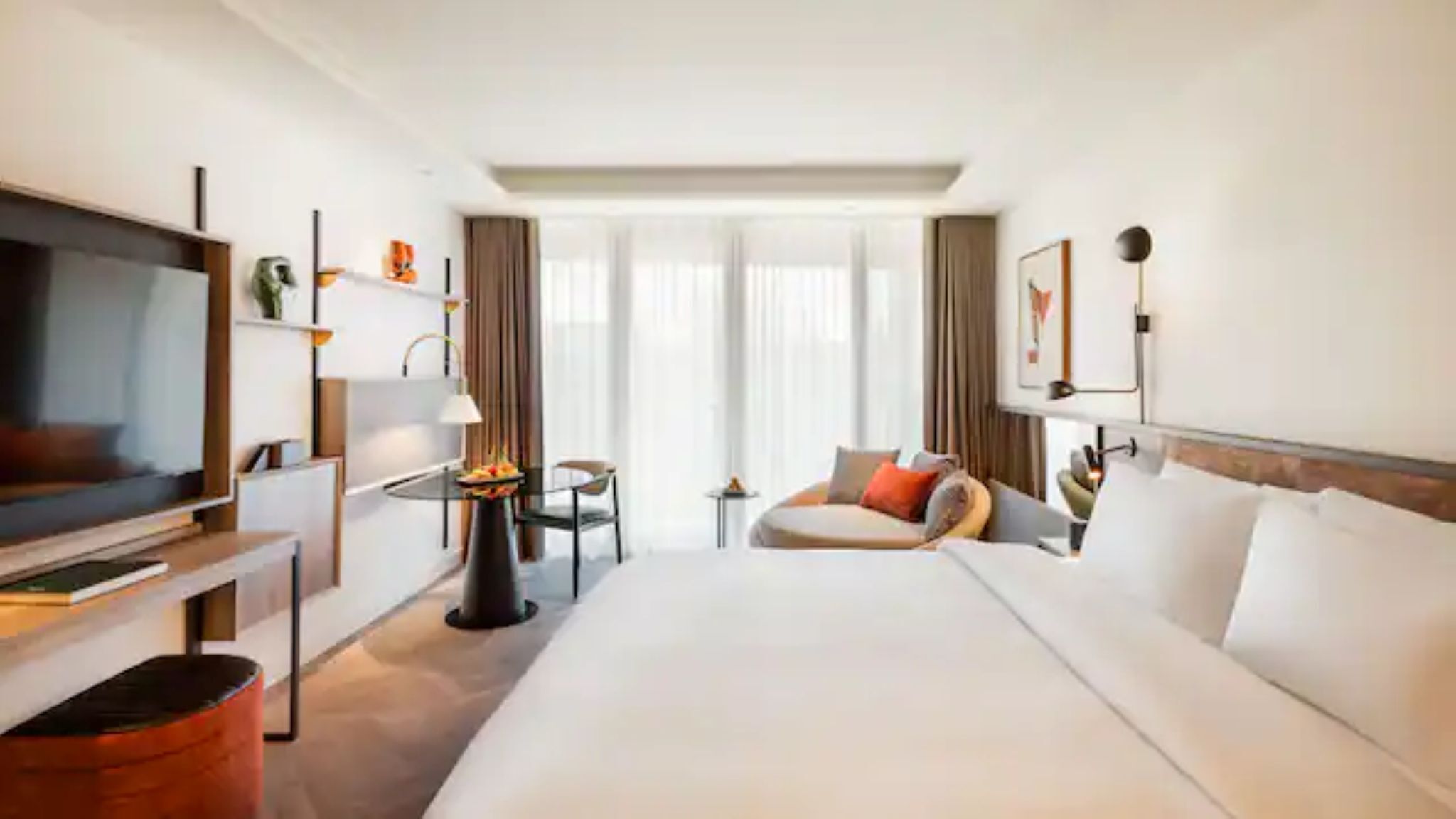 Habitación de hotel con una cama grande, televisión, escritorio con lámpara, una mesita con un florero y vistas al exterior.