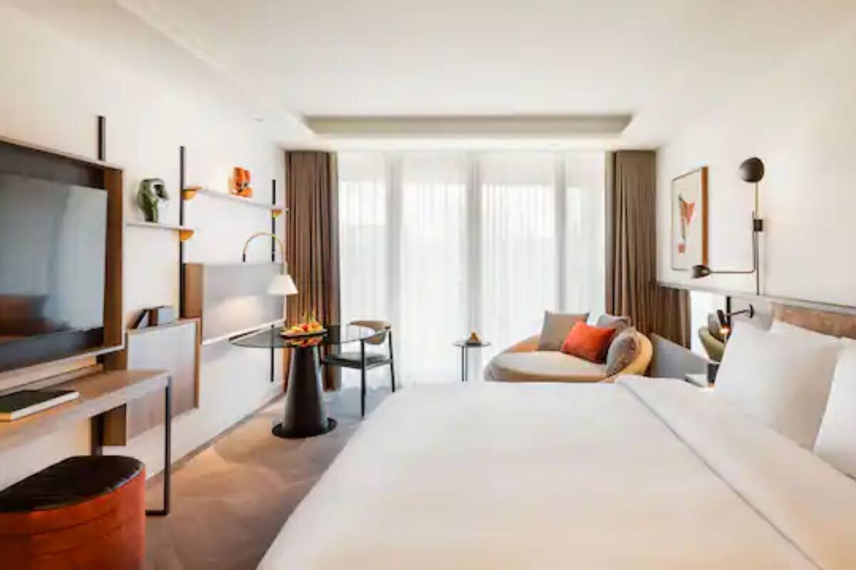 Habitación de hotel con una cama grande, televisión, escritorio con lámpara, una mesita con un florero y vistas al exterior.