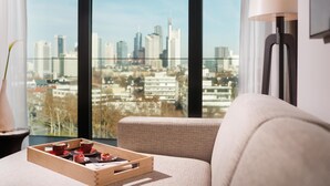 A modern living room with a city view, a wooden tray with cups, and a lamp. - Kennedy 89 Hotel Frankfurt, part of Hyatt (Frankfurt)