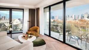 Un salón moderno con sofá, mesa de centro y una silla. Se ve un ventanal con vistas a la ciudad.