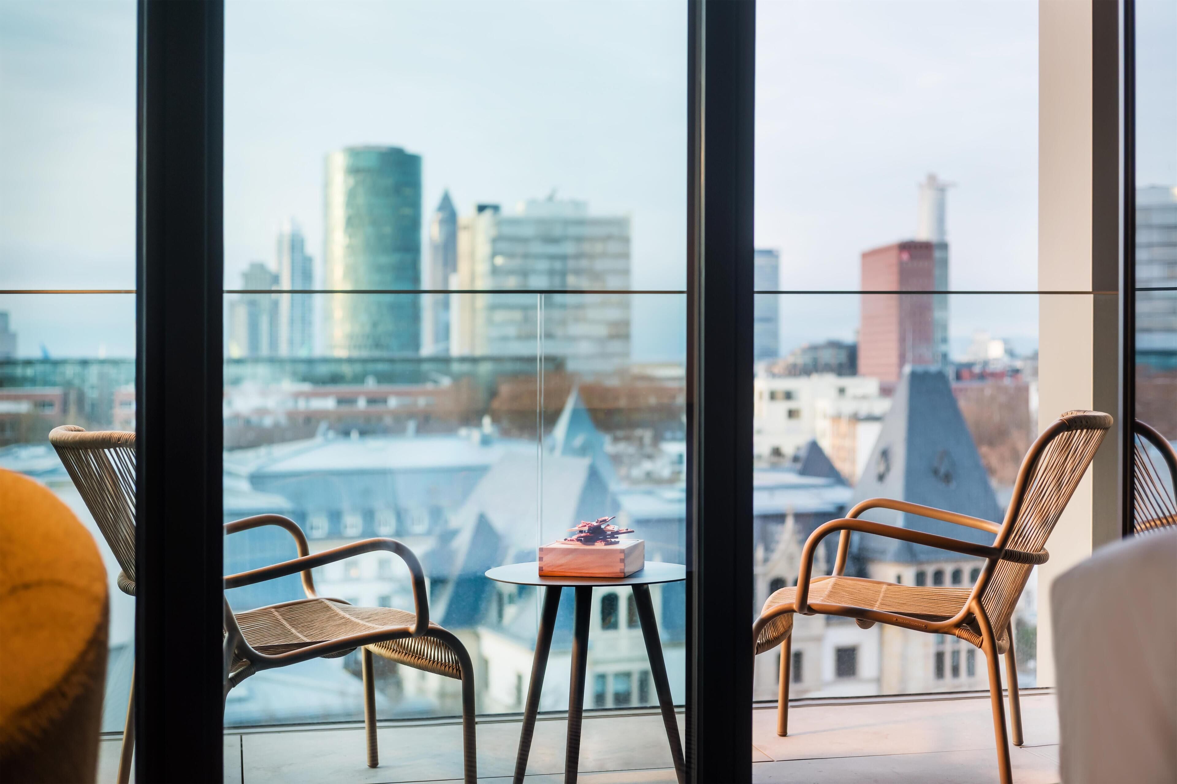 A balcony with wicker chairs, a small round table, and a city view.