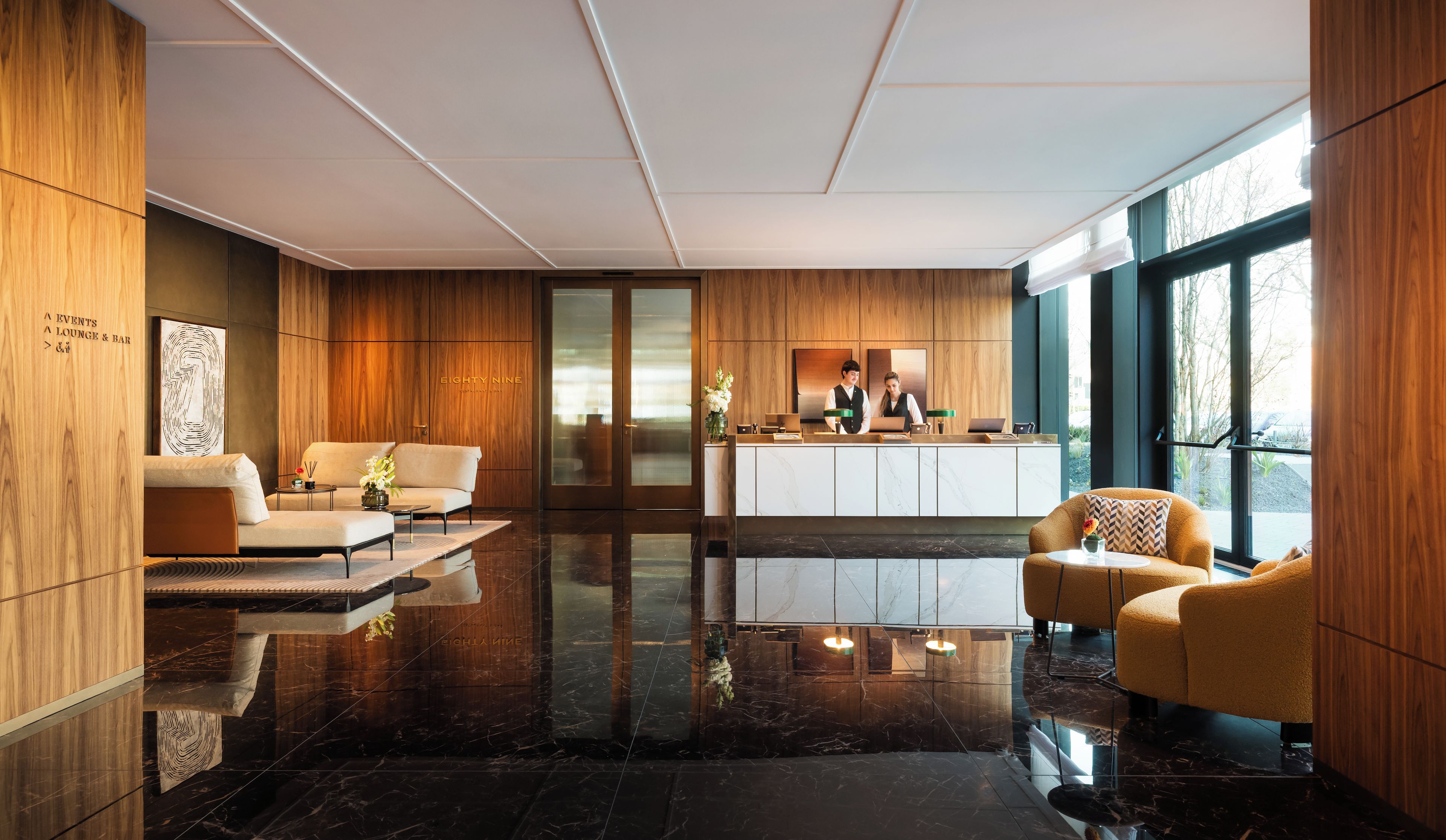A modern lobby with a reception desk, seating area, and large windows.