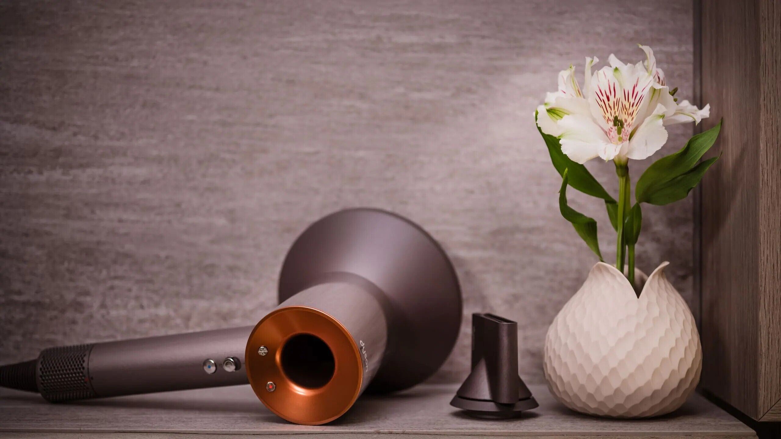 A microphone, a speaker, and a vase with a flower on a wooden surface.