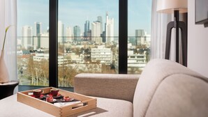 Una sala de estar moderna con vista a la ciudad, un sofá, una bandeja con tazas y una lámpara.