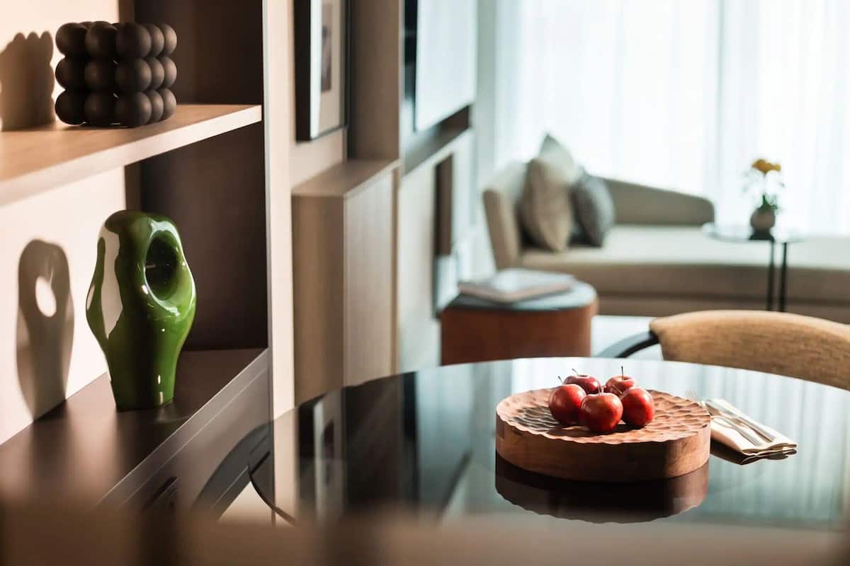 Una sala moderna con una mesa redonda de madera, un florero verde y un cuenco de madera con frutas.