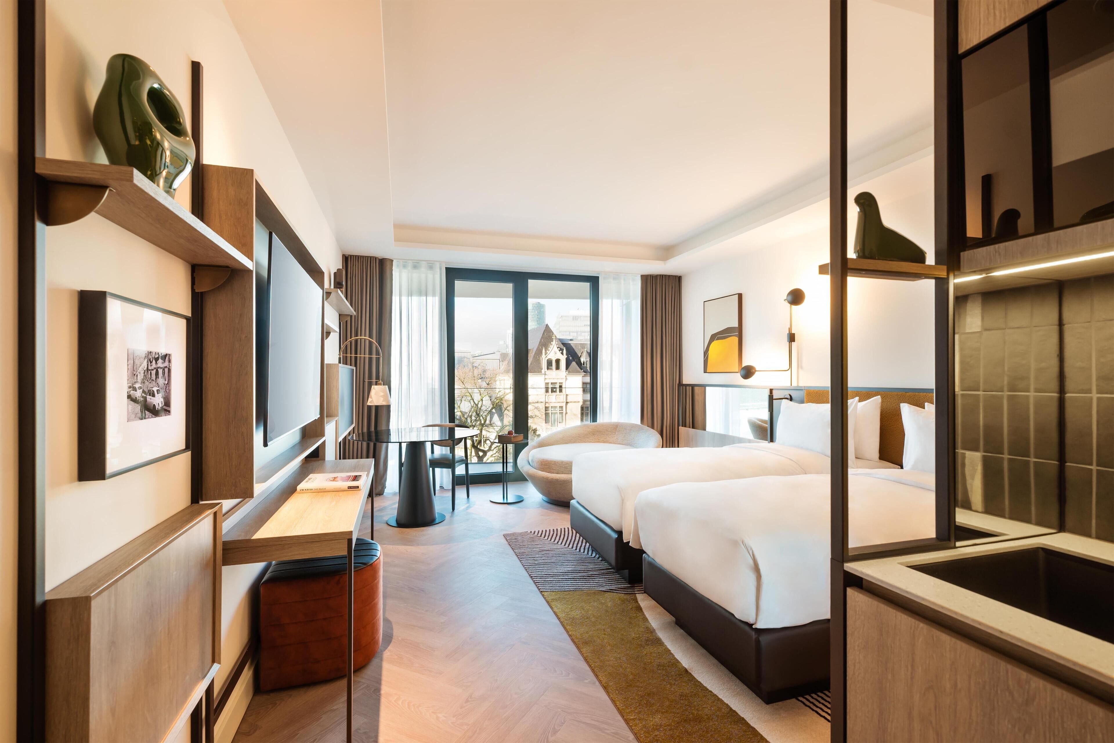Quarto de hotel moderno com uma cama grande, uma escrivaninha e vista para a cidade.