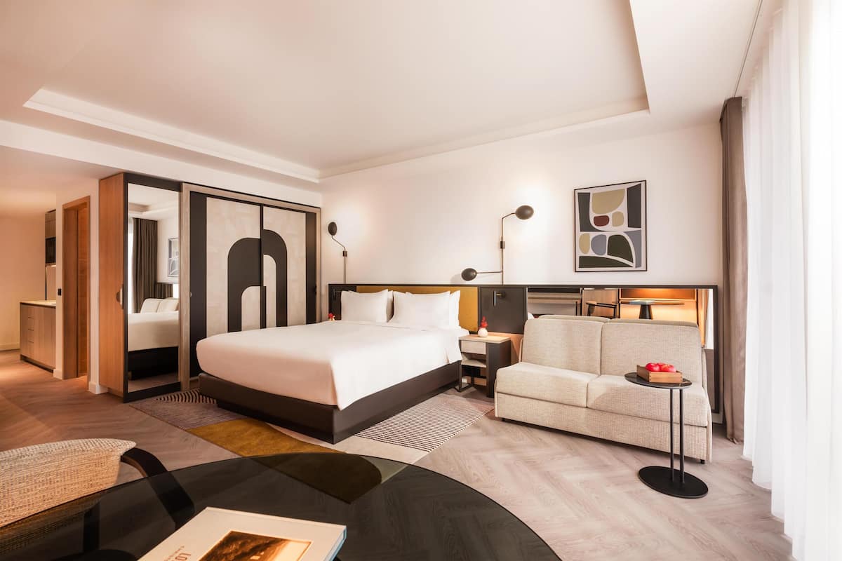 Una habitación de hotel moderna con una cama grande, un sofá, una mesita y un escritorio.