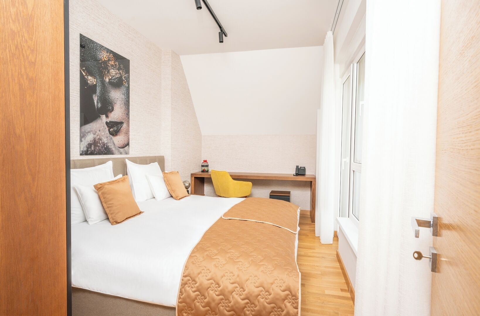 A bedroom with a bed, a desk, a chair, and a large painting on the wall.