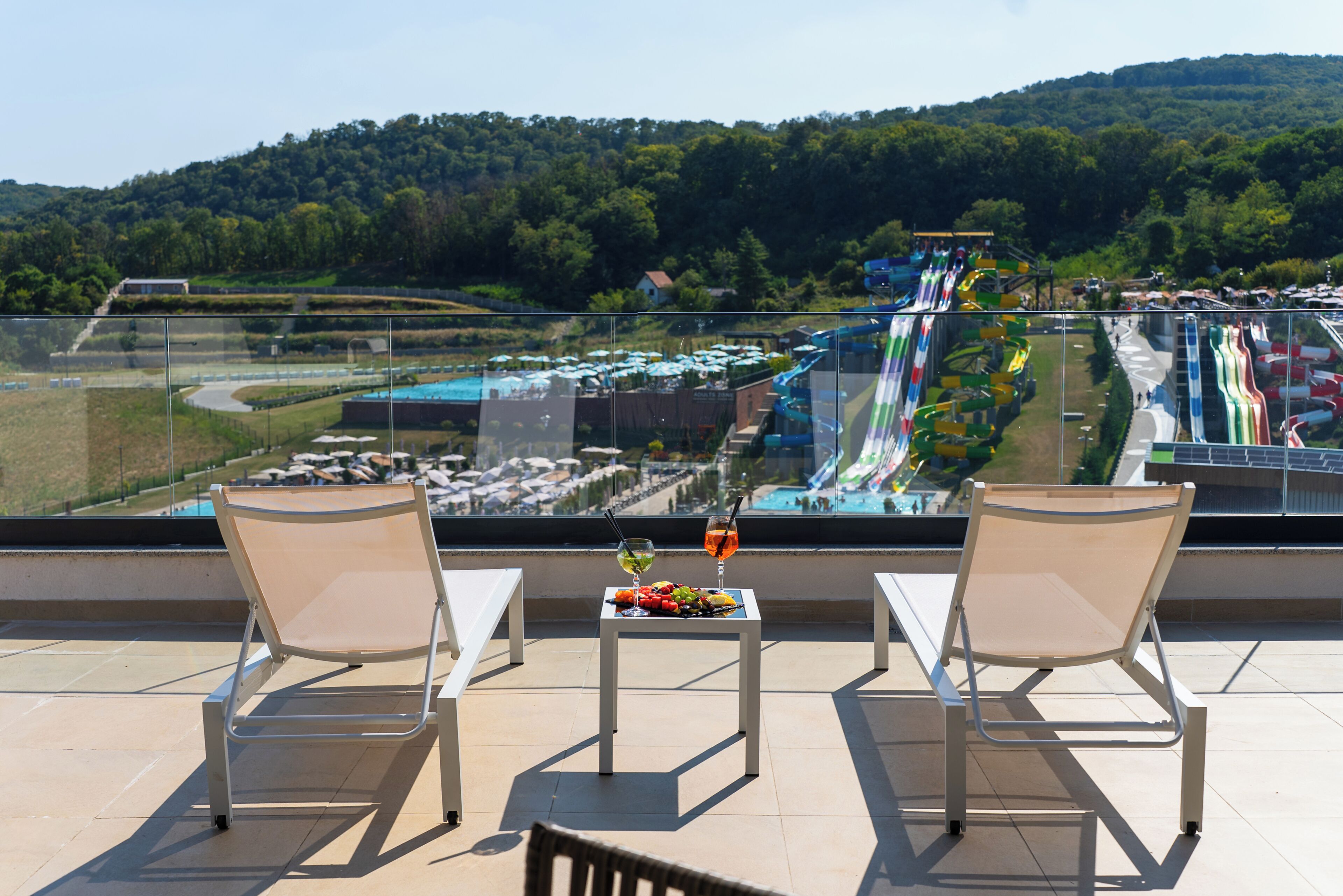 Un balcon avec deux chaises et une table, donnant sur un parc aquatique avec des toboggans et des piscines.