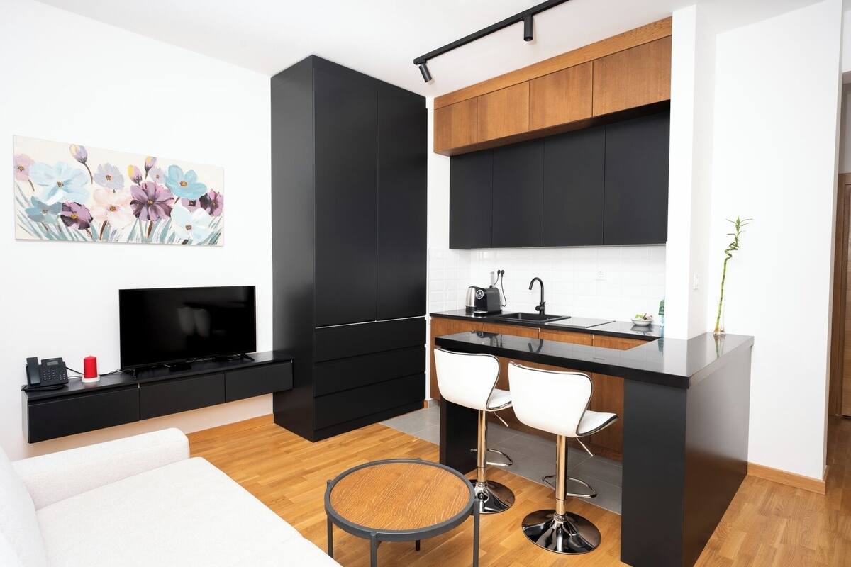 Une cuisine moderne avec des meubles noirs, un plan de travail en bois et un évier noir. On y trouve un téléviseur posé sur un meuble noir, un téléphone rouge et un tableau représentant des fleurs accroché au mur.