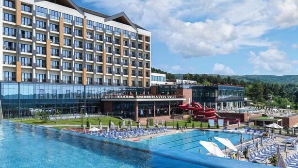 A hotel with a large pool, a water slide, and a mountain backdrop.