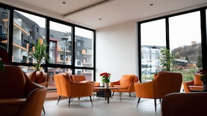 A modern hotel lobby with large windows, orange seating, and a potted plant.