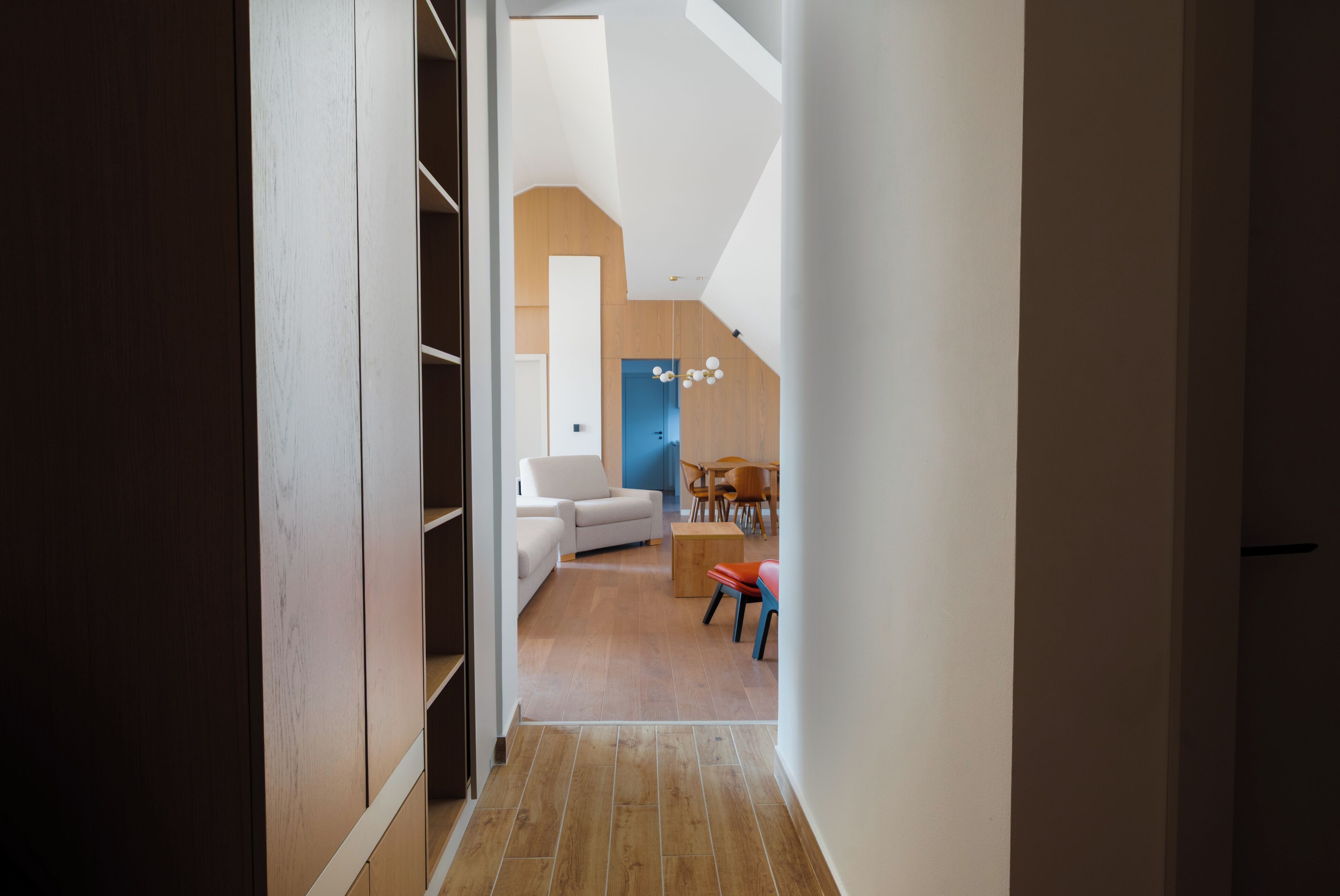 A narrow hallway leading to a living area with a sofa, a dining table, and chairs.