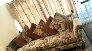 Um sofá com estofamento floral e almofadas castanhas em um quarto com porta e cortinas.