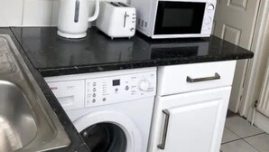 Uma cozinha compacta com armários brancos, bancada preta, máquina de lavar Bosch, torradeira e micro-ondas.