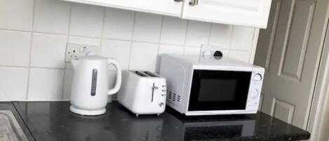 A compact kitchen with white cabinets, a black countertop, a Bosch washing machine, a toaster, and a microwave.