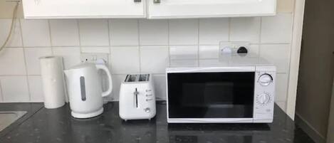 Eine Küche mit weißen Schränken, einem Toaster, einem Wasserkocher und einer Mikrowelle auf einer schwarzen Arbeitsplatte.