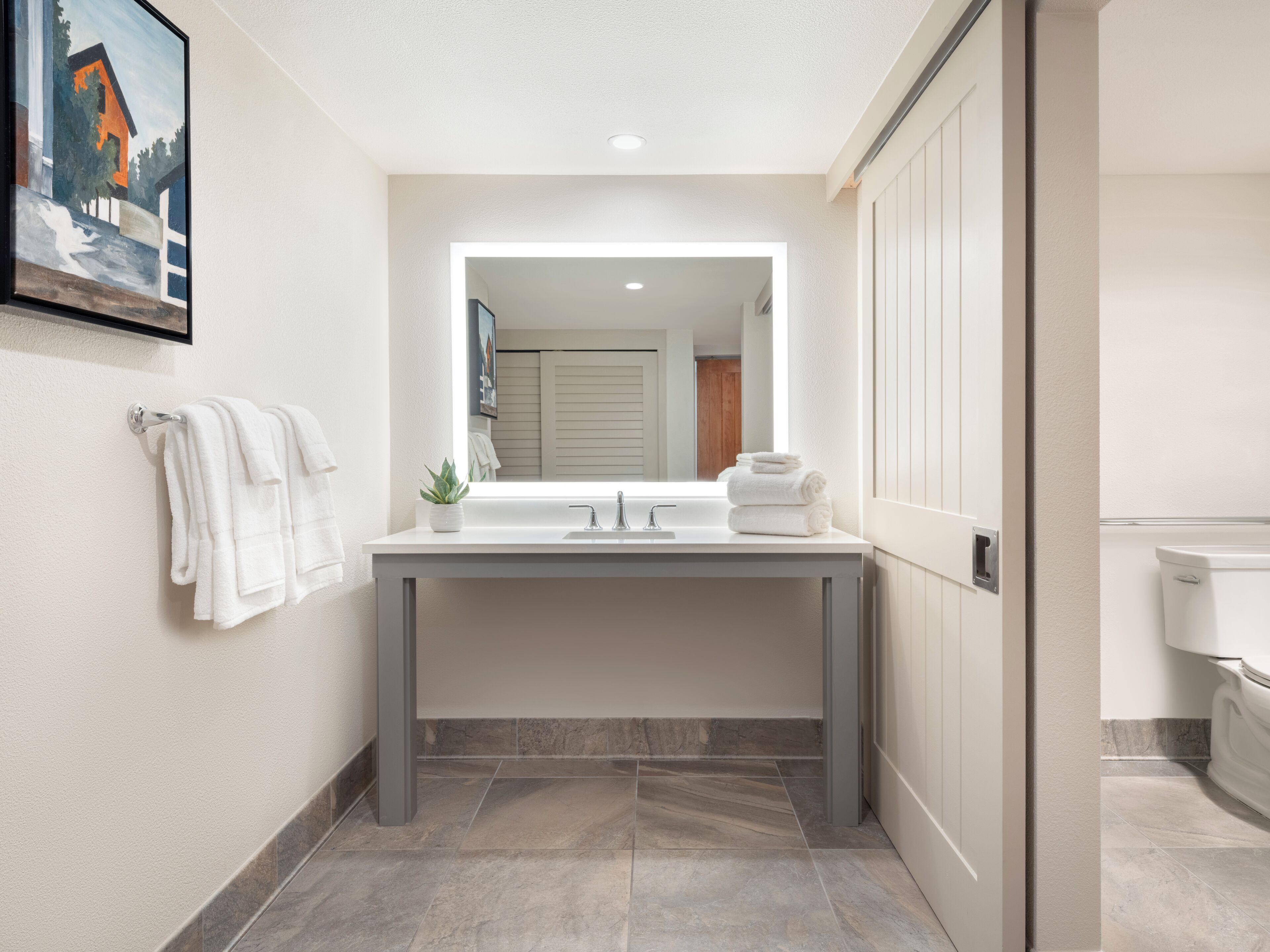 Un baño moderno con un espejo grande, lavamanos blanco y un inodoro.