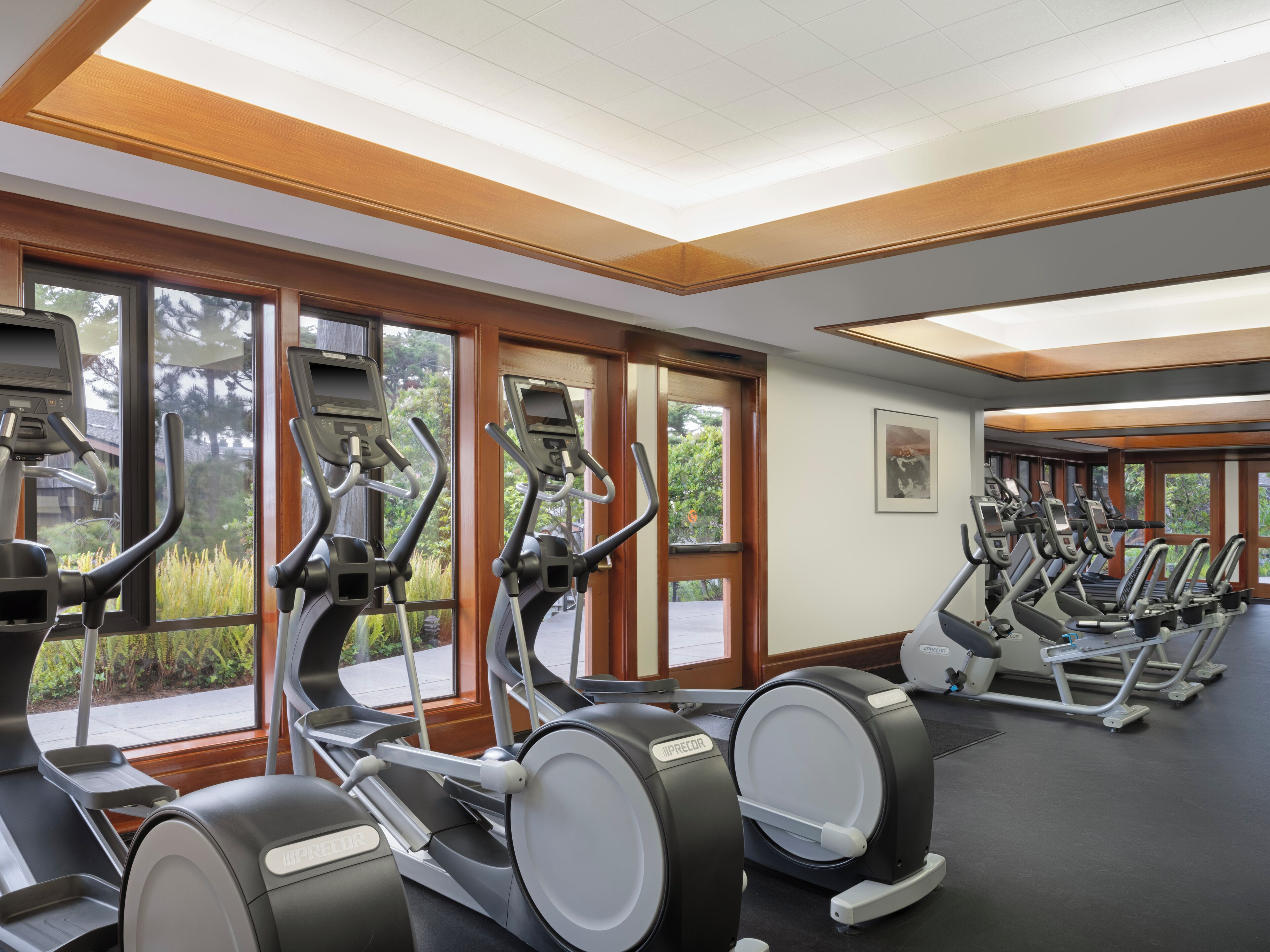 A gym with multiple treadmills, large windows, and a ceiling with recessed lighting.
