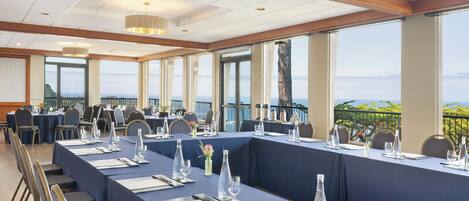 A conference room with a long table set for a meeting, large windows with a view of the sea, and a balcony with a railing.