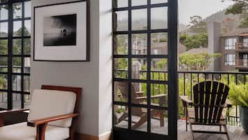 Ein Zimmer mit Holzstuhl, einem gerahmten Bild an der Wand und Blick auf einen Balkon mit Gartenmöbeln und Bepflanzung.