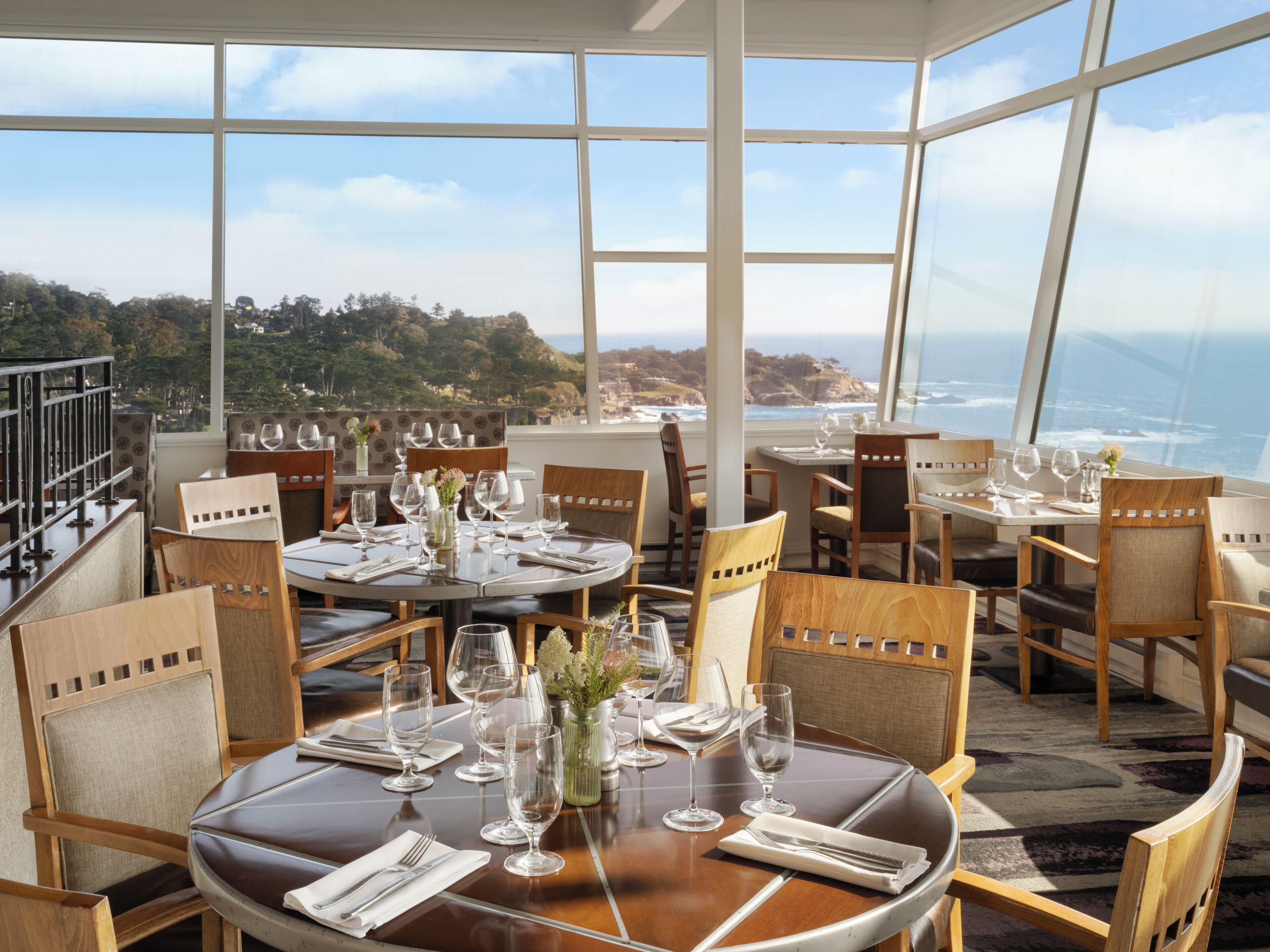 A restaurant with round tables and chairs, large windows, and a view of the ocean.