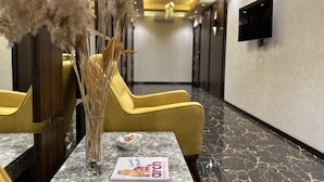 A hotel lobby with a reception desk, yellow chairs, a vase with dried flowers, a guest book, and a television on the wall. - Arch Apart Hotel (Yerevan)