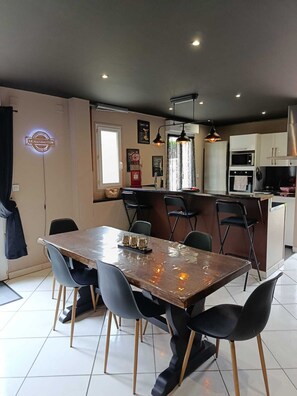 A modern kitchen with a dining area, featuring a central island, pendant lighting, and a visible sign on the wall.