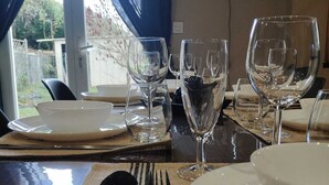 A dining table set with white plates, cutlery, and wine glasses, with a view of greenery outside.
