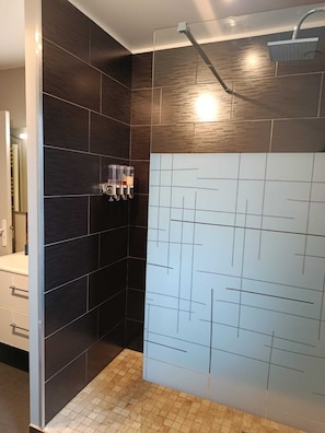 A modern bathroom with dark tiles, a shower with a handheld showerhead, and a glass partition with a geometric pattern. - LE Manhattan Authentique Maison Climatisée de 75 m² (Brasles)