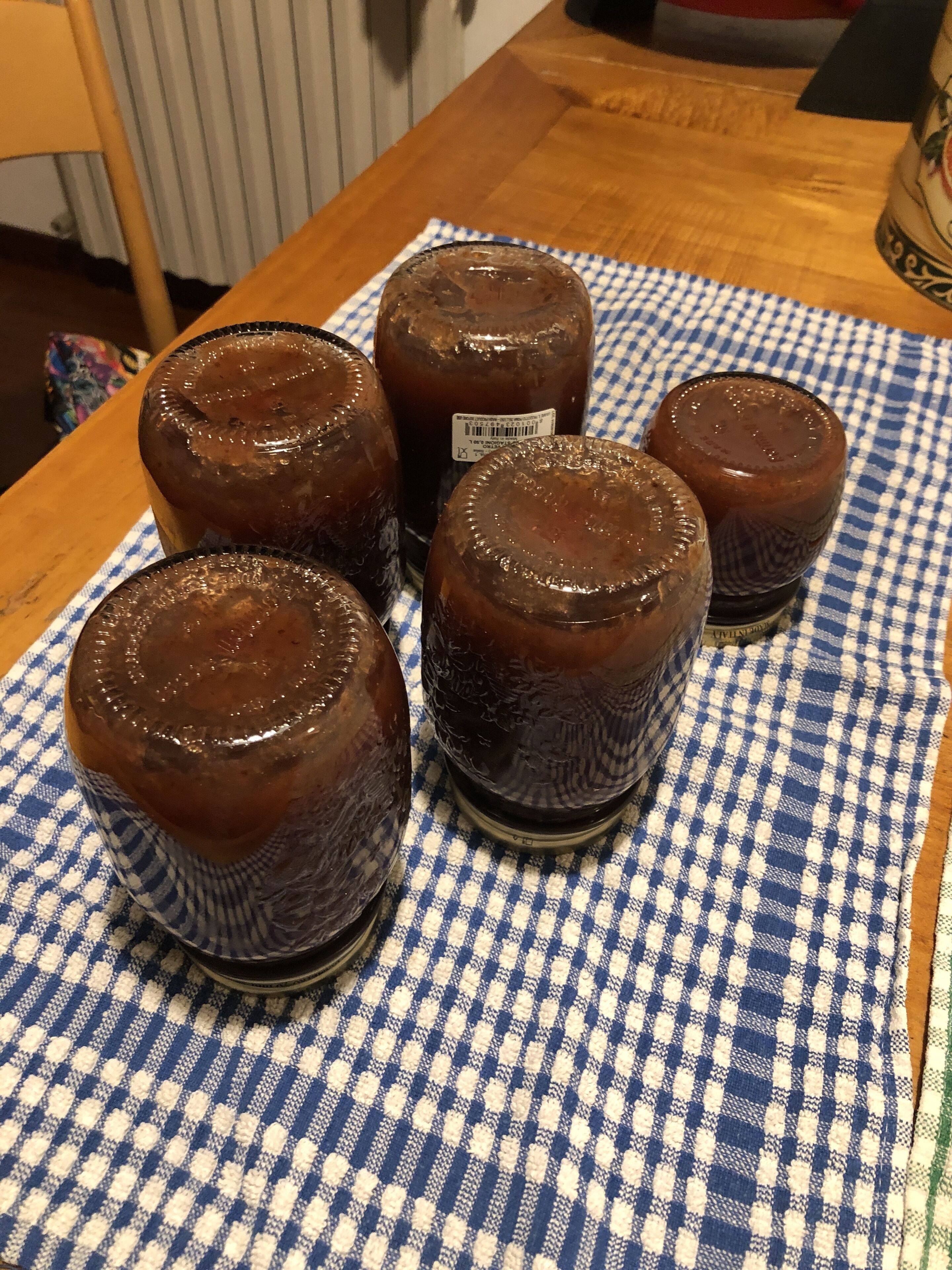 Five glass jars with a dark liquid on a blue and white checkered cloth.
