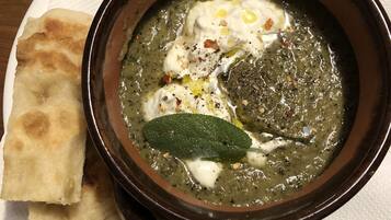 Un tazón de sopa con una cucharada de crema y una hoja verde encima, acompañado de un trozo de pan plano sobre un plato blanco.