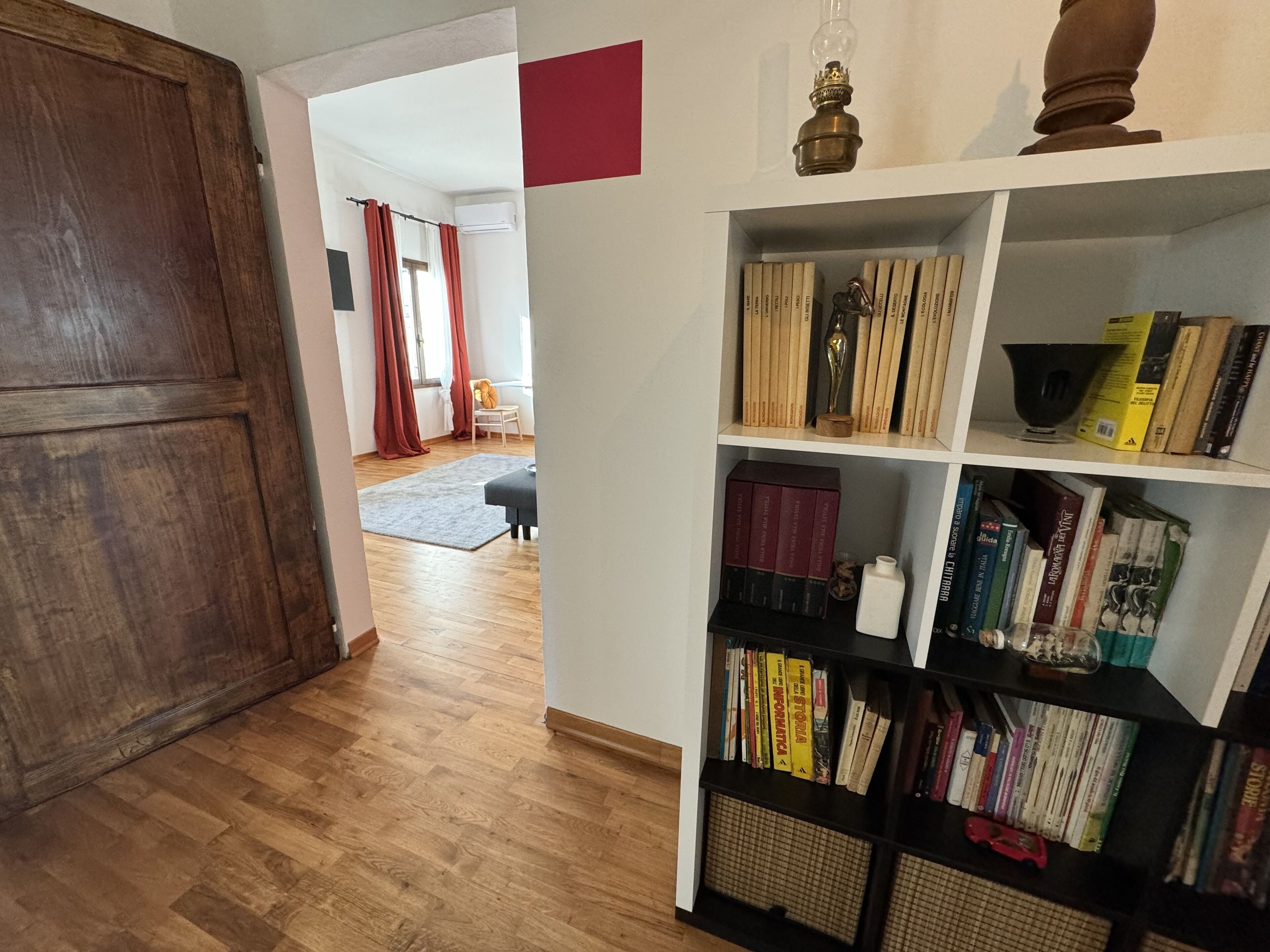 Un corridoio con pavimento in legno, una libreria piena di libri e una porta che dà su un'altra stanza.
