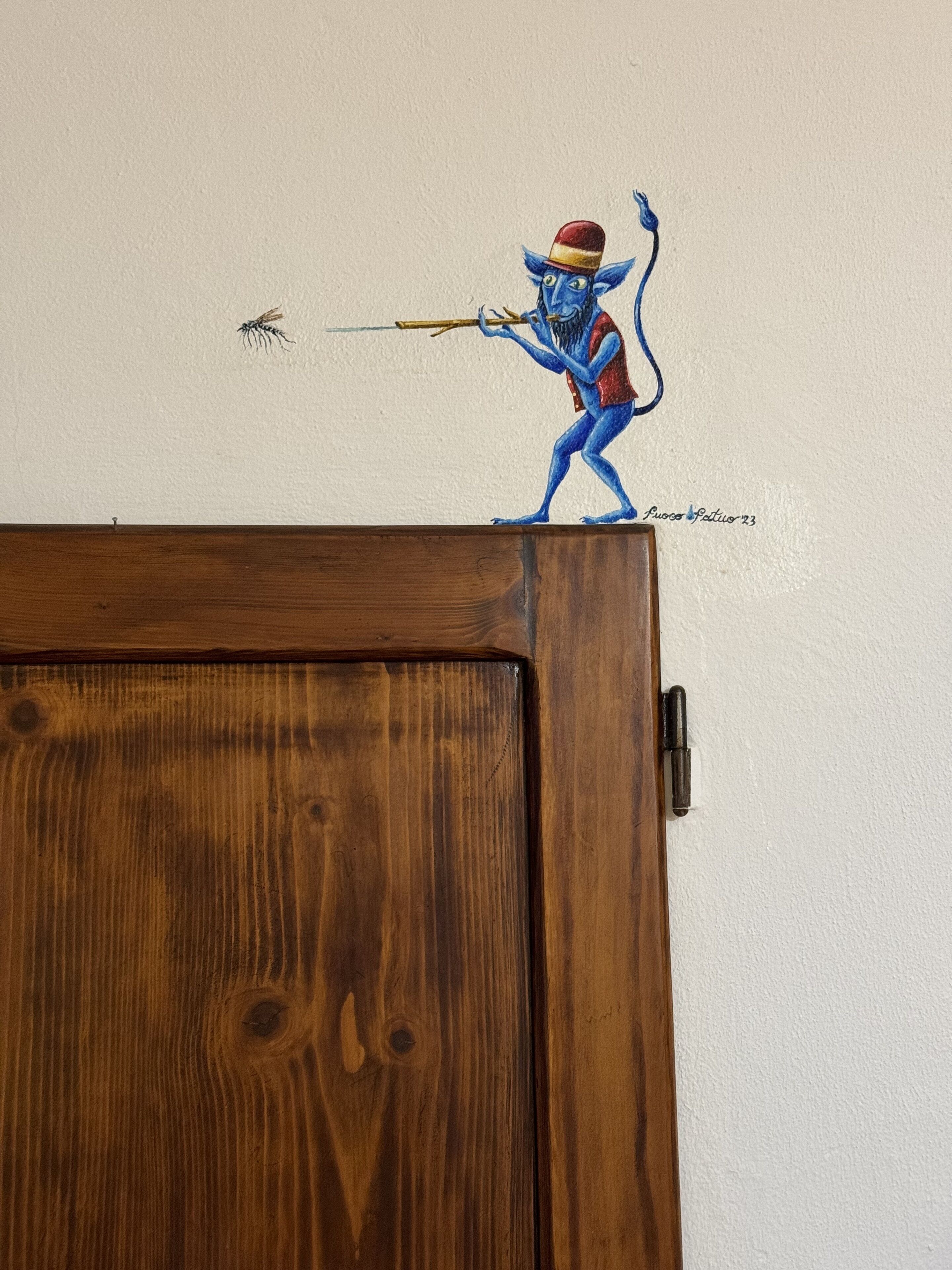 Een houten deur met een blauw figuur van een wezen geschilderd op de muur erboven.