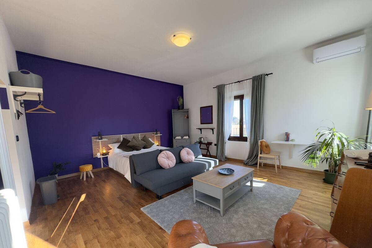 A modern living room with a purple accent wall, a sofa, a coffee table, and a dining area with a plant.