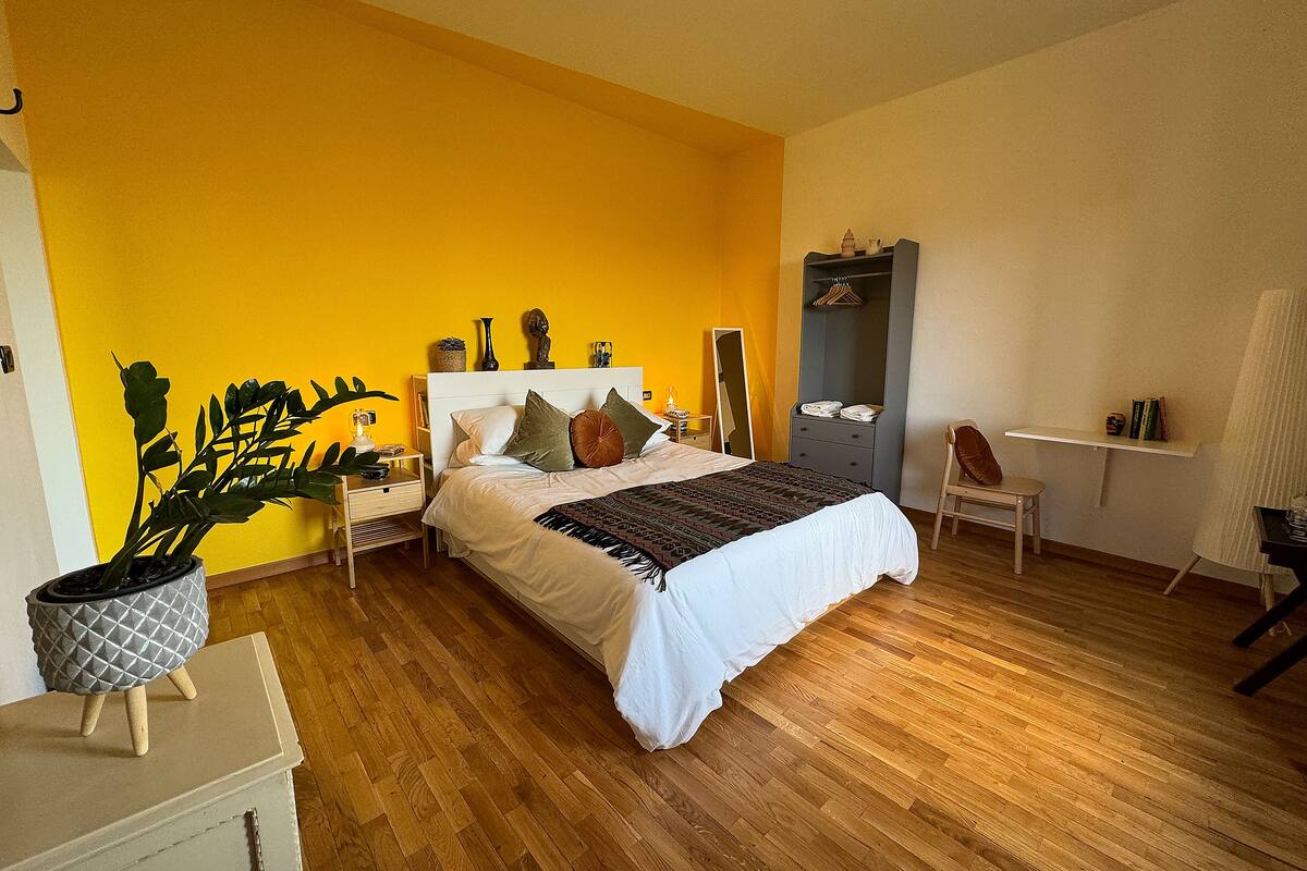 A bedroom with a bed, bedside tables, a chair, a wardrobe, and a potted plant.