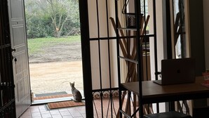 A room with a tiled floor, a desk with a laptop, a chair, a window with a view of trees, and a door with a metal gate. - Affittacamere Ca' da Mazapedar (Lugo)