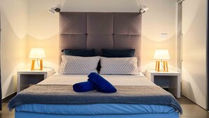 Ein modernes Schlafzimmer mit einem großen Bett, zwei Nachttischen mit Lampen, einer gesteppten Kopfteil und einer neutralen Farbgestaltung.