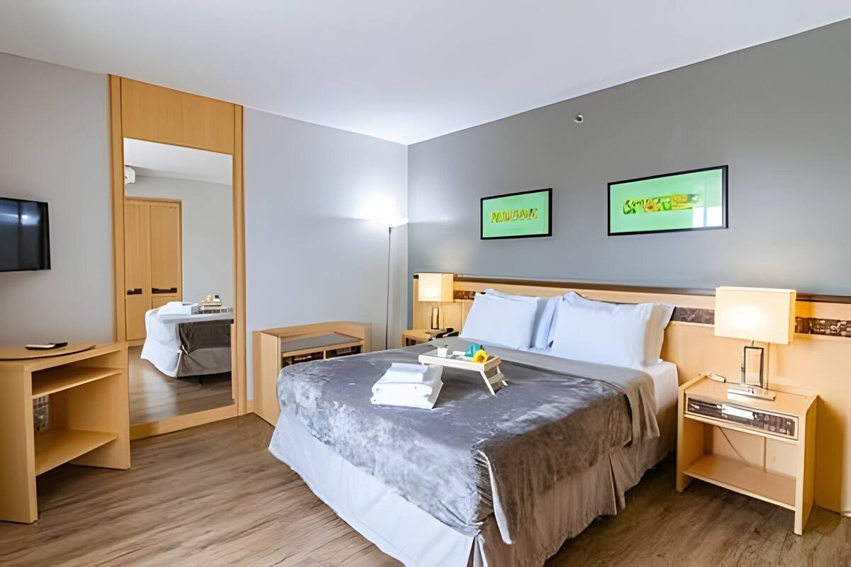 A hotel room with a bed, bedside tables, a desk, a TV, and two framed pictures on the wall.