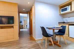 A modern kitchen with a dining area, wooden cabinets, a flat-screen TV, and a microwave.