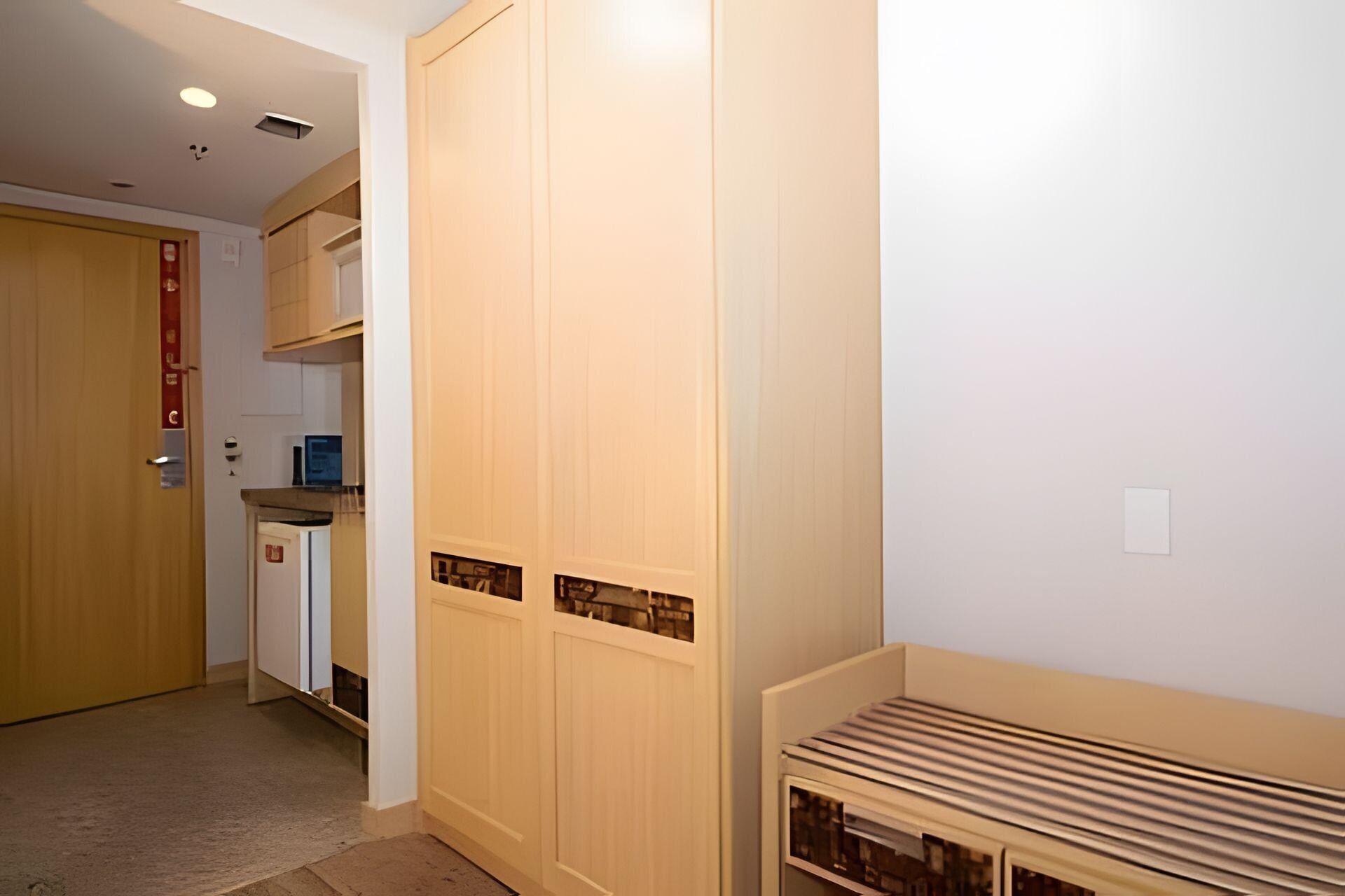 Un couloir avec une armoire en bois, un radiateur et une porte ornée d’une enseigne rouge.