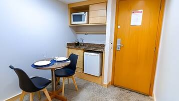 A small kitchenette with a microwave, a refrigerator, and a sink. There is a dining table with chairs and a small cabinet above it.